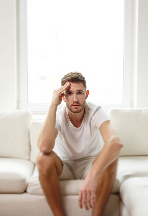 Мужчина сидит и держится правой рукой за голову